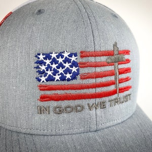 May include: A gray and red baseball cap with an embroidered American flag and the words "In God We Trust".