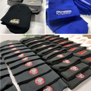 May include: A stack of black knit beanies with a red and white logo that says "South Pittsburgh Rebellion" in a circle. The beanies are stacked on a white surface.