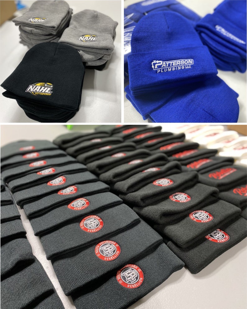 May include: A stack of black knit beanies with a red and white logo that says "South Pittsburgh Rebellion" in a circle. The beanies are stacked on a white surface.
