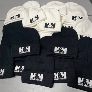 May include: A pile of black and white knit beanies with the text "H&H Lawn Service" embroidered on each one.