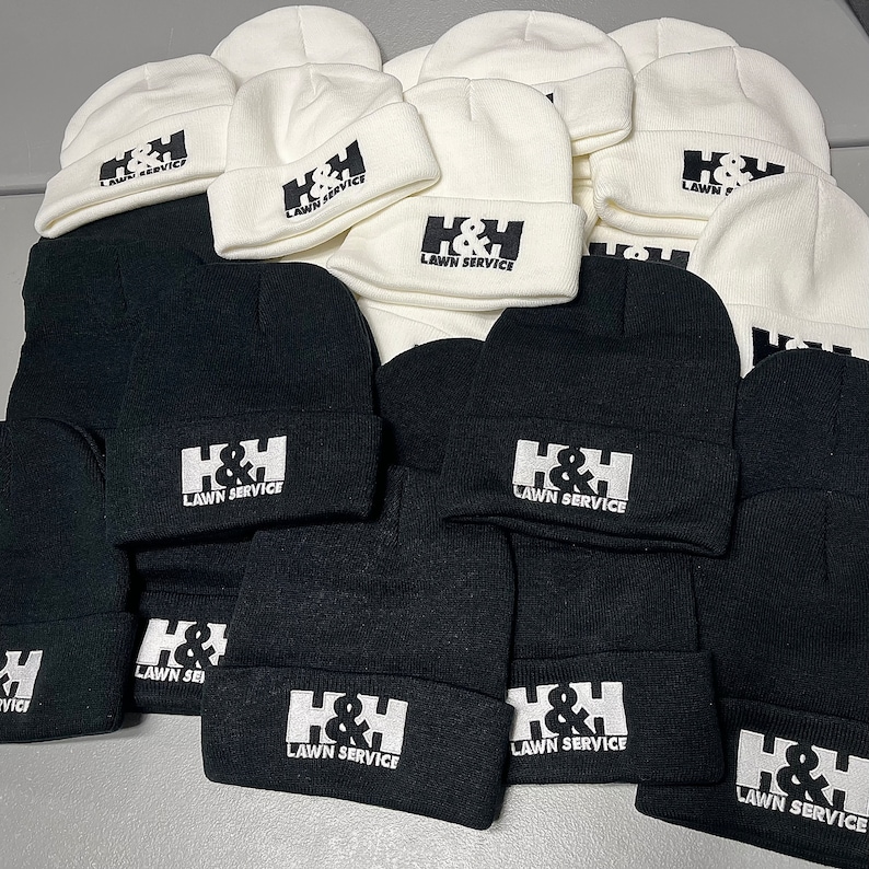 May include: A pile of black and white knit beanies with the text "H&H Lawn Service" embroidered on each one.