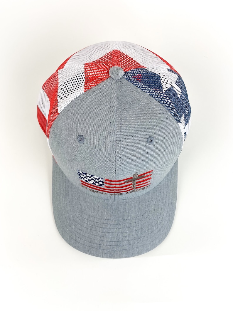 May include: A gray and blue mesh trucker hat with a red, white, and blue American flag design on the front. The flag has a cross on it and the words "God First" are embroidered below it.