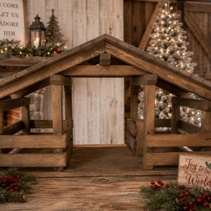 May include: A wooden nativity stable featuring a dark brown stained finish, a gabled roof, and open sides with horizontal slat railings. The structure is constructed from thick, rustic timber beams, creating an open-air shelter design.