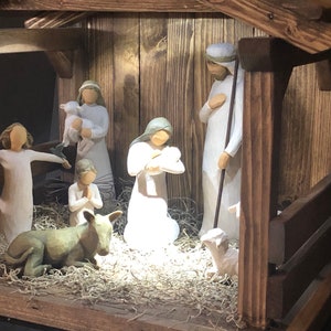 May include: A wooden nativity scene featuring figurines of Mary, Joseph, baby Jesus, angels, and animals. The figures are in white robes and are set in a rustic wooden stable with straw bedding. A religious Christmas decoration.