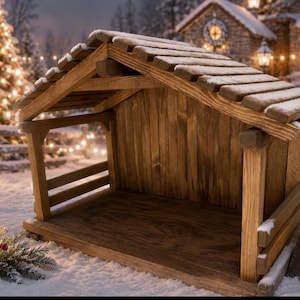 May include: A wooden nativity stable featuring a gabled roof with horizontal slats, a flat base, and vertical wall planks. A small rectangular sign stands to the right with the text O Come Let Us Adore Him written in white script lettering.