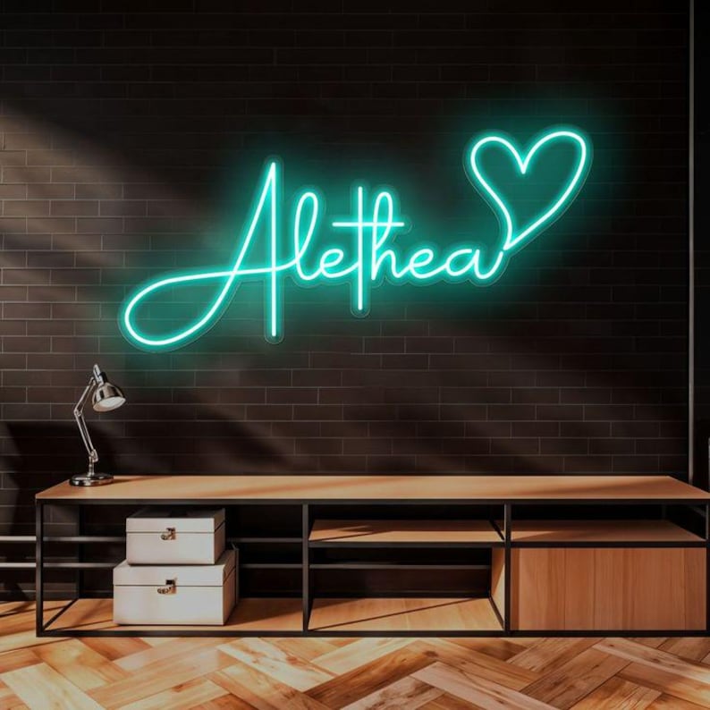 May include: A teal neon sign displaying the name "Alethea" in a cursive font, with a heart symbol at the end. The sign is mounted on a dark brick wall above a wooden console with storage boxes and a desk lamp.