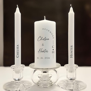 May include: A wedding unity candle set featuring a white pillar candle and two taper candles. The pillar candle has the names "Chelsea & Hunter" and the date "11. 26. 2024". The taper candles are labeled "Chelsea" and "Hunter". The candles sit in clear glass holders.