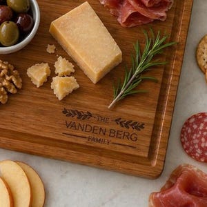 K&ouml;nnte beinhalten: Ein Holz-Charcuterie-Brett mit Trauben, K&auml;se, Oliven, Salami und Crackern. Das Brett ist mit "THE VANDEN BERG FAMILY" graviert. Ein Messer und kleine Schalen mit Marmelade und Oliven sind ebenfalls vorhanden. Das Brett misst ca. 30 cm x 40 cm.