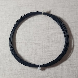 Puede incluir: Un haz circular de hilo negro, asegurado con una brida de plástico blanco. El hilo está bien enrollado, formando un círculo limpio. El fondo es una superficie clara y texturizada.