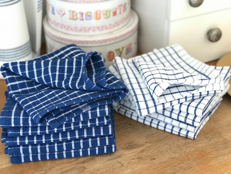 May include: Two stacks of blue and white checkered kitchen towels. The towels are folded and stacked on a wooden surface.