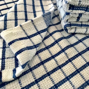 May include: A white kitchen towel with a blue checkered pattern. The towel is folded and stacked on top of another towel.