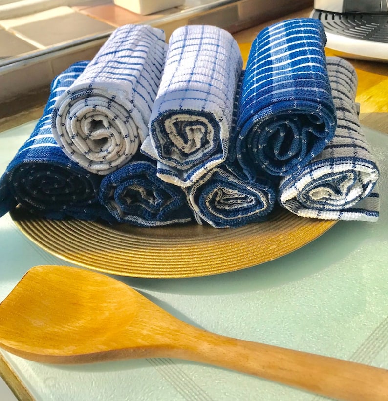 May include: A set of six blue and white striped kitchen towels rolled up and arranged on a gold-colored plate. The towels are made of a soft, absorbent fabric and are perfect for drying dishes, hands, and surfaces.