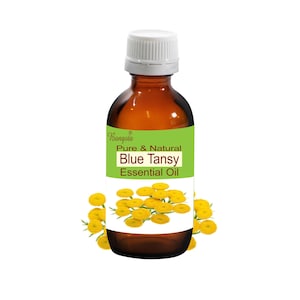 Op de afbeelding: Een bruine glazen fles met een witte dop, met het label "Bangoia Pure & Natural Blue Tansy Essential Oil". De fles is omringd door gele bloemen.