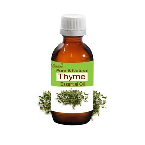 May include: A brown glass bottle with a white cap, labelled "Thyme Essential Oil." The label is green and white, with the brand name "Bangola." Fresh thyme sprigs are arranged around the bottle. The bottle appears to be approximately 10 cm tall.