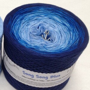 K&ouml;nnte beinhalten: Eine Kn&auml;uel blaues Ombre-Garn namens "Song Song Blue" mit einem wei&szlig;en Etikett, auf dem "200g Laufl&auml;nge ca 760m - 50% Baumwolle 50% Polyacryl" steht.