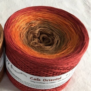 May include: A skein of yarn in a gradient of red, orange, and brown colors. The yarn is labeled "Cafe Oriental" and "200g Lauflange ca 1000m - 50% Baumwolle".