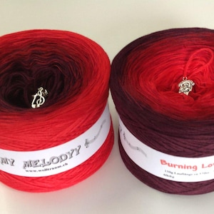 May include: Two skeins of ombre yarn, one red to dark purple and one burgundy to red. The yarn is labeled "My Melody" and "Burning Love".