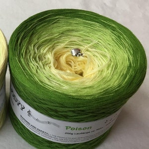 May include: A skein of green and yellow ombre yarn with a silver heart charm. The yarn is labeled "Poison" and "200g Lauffange ca 750m".
