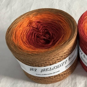 May include: A skein of brown, orange, and red yarn with a gradient color pattern. The yarn is wound into a ball and has a label that reads "My Melody" and "www.wolltraum.ch/com".