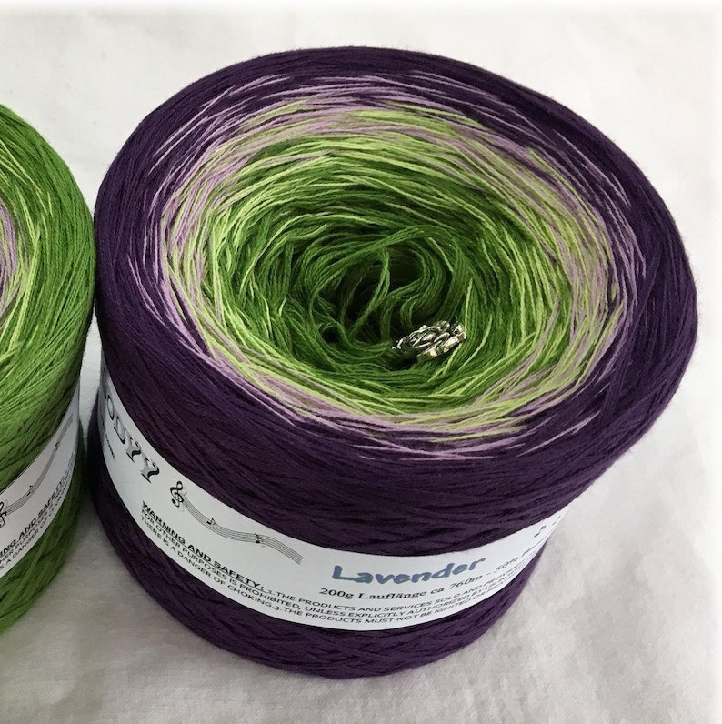 May include: A skein of purple, green and pink ombre yarn with the label "Lavender 200g Lauflange ca 700m 100% Baumwolle" on the side.