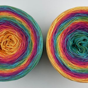 May include: Two skeins of rainbow colored yarn wound into balls. The yarn is a gradient of yellow, orange, red, purple, blue, green, and yellow.