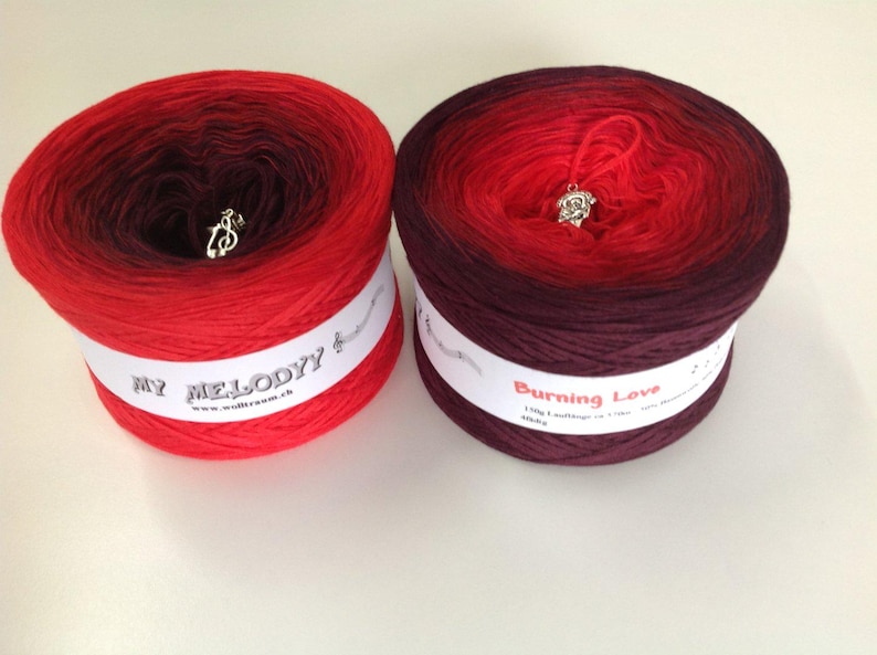 May include: Two skeins of ombre yarn, one red to dark purple and one burgundy to red. The yarn is labeled "My Melody" and "Burning Love".