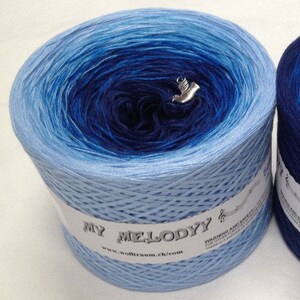 K&ouml;nnte beinhalten: Eine Kn&auml;uel blaues Ombre-Garn mit einem wei&szlig;en Etikett, auf dem "My Melody" und eine Website-Adresse stehen. Das Garn ist zu einer Kugel gewickelt und hat einen silbernen Anh&auml;nger.