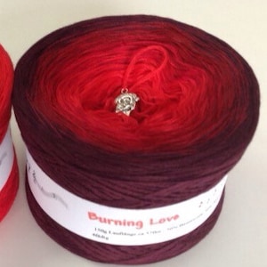 May include: A skein of red and burgundy ombre yarn with a silver charm attached. The yarn is labeled "Burning Love" and is 150g.