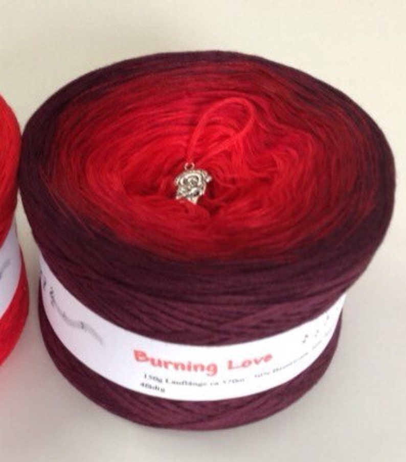 May include: A skein of red and burgundy ombre yarn with a silver charm attached. The yarn is labeled "Burning Love" and is 150g.