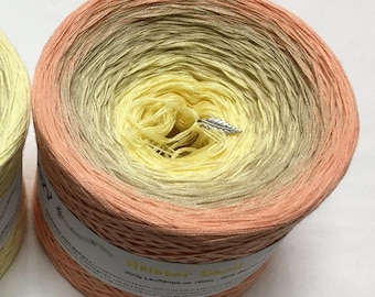 May include: A ball of yarn in a peach, yellow, and beige ombre colorway. The yarn is wound around a cardboard tube with a label that reads "Heißer Sand" and "200g Lauflange ca 750m - 50m = ca 15 sts".