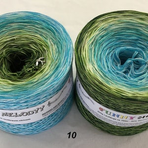May include: Two skeins of yarn in shades of blue and green, with a gradient effect. Each skein has a small charm attached. The yarn is labeled "MY MELODYY" and "FUNNY NO.". The number "10" is printed on the bottom.