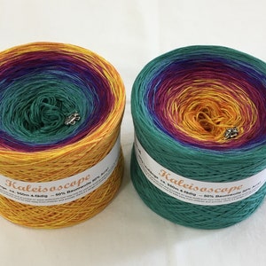 Puede incluir: Dos ovillos de hilo Kaleidoscope, cada uno en un degradado de color diferente. El hilo es un degradado de amarillo, naranja, rojo, morado, azul y verde. Los ovillos están etiquetados "Kaleidoscope ca. 900m 4-fädig 50% Baumwolle 50% Acryl"