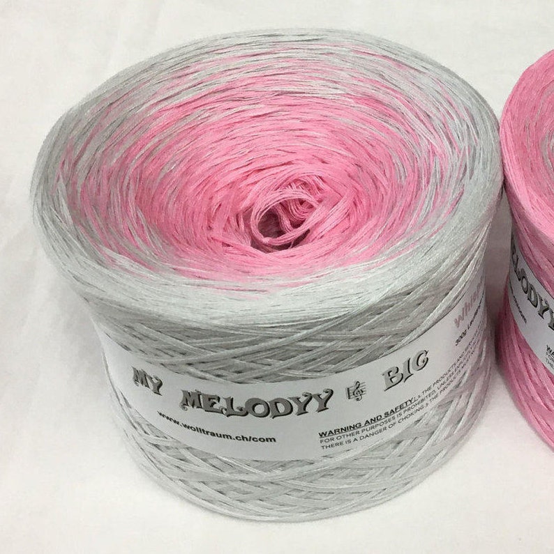 May include: A skein of pink and gray yarn with the text "MY MELODYY BIG" and "www.wolltraum.ch/com" on the label. The yarn is wound into a ball shape.