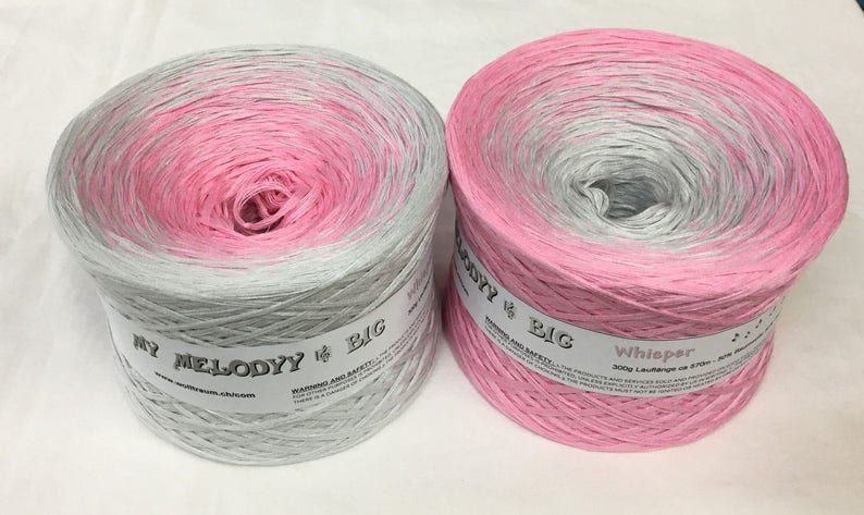 May include: Two skeins of ombre yarn, one in pink and grey and the other in grey and pink. The yarn is labeled "My Melody # Big" and "Whisper 300g Laufl&auml;nge ca. 570m."