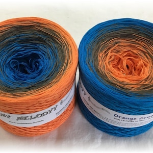 Puede incluir: Dos ovillos de hilo, uno naranja, azul y negro degradado y el otro azul, naranja y negro degradado. Los ovillos están etiquetados como "My Melody" y "Orange Crush".