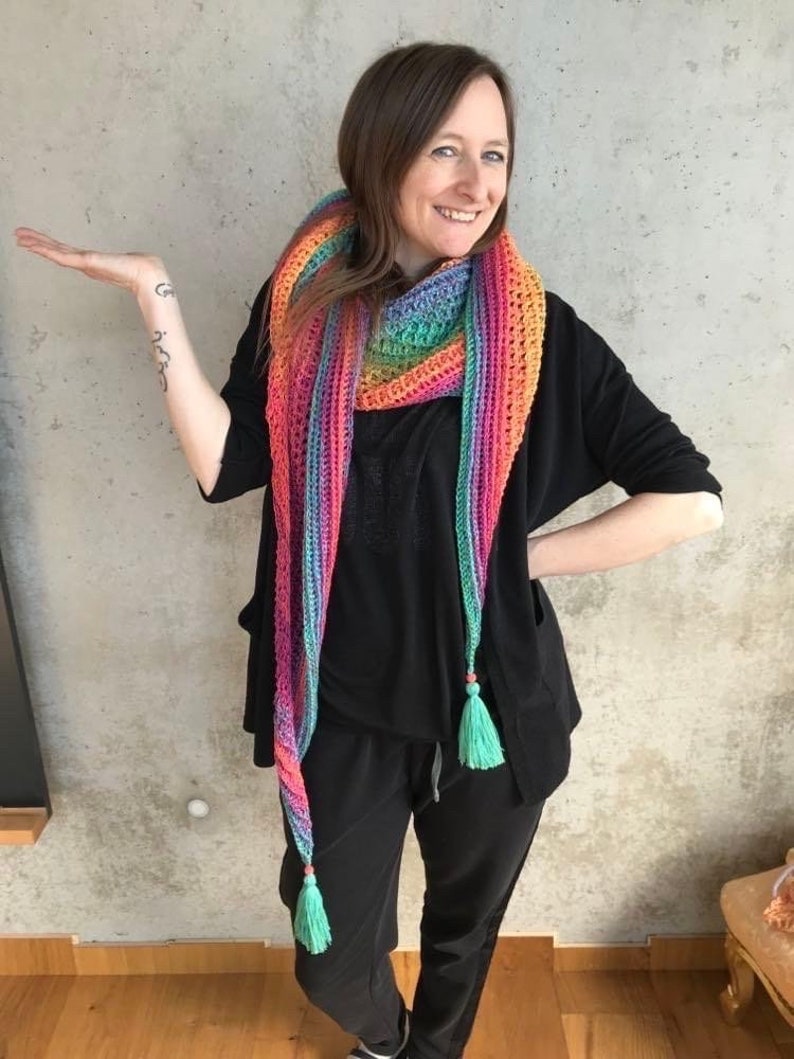 May include: A long, colorful crochet scarf with a rainbow gradient of pink, orange, yellow, green, blue, and purple. The scarf has two long tassels at the ends, which are a bright turquoise color.
