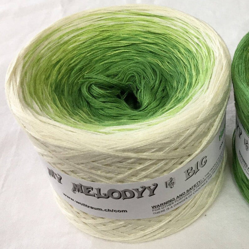 May include: A skein of green and white ombre yarn with the label "MY MELODYY BIG" and the website address "www.wolltraum.ch/com".