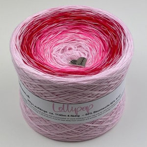 May include: A large spool of Lollipop yarn in shades of pink and red, with a silver heart-shaped charm. The yarn is a gradient of colors, transitioning from light pink to deep red. The label indicates the yarn is 50% cotton and 50% acrylic.