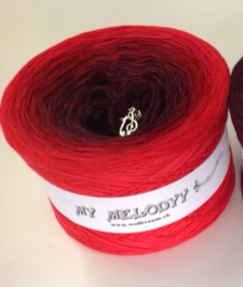 May include: A skein of red and burgundy ombre yarn with a white label that reads "My Melody" and a silver music note charm.
