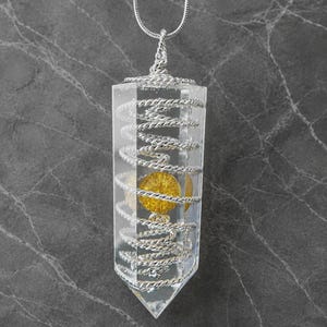 May include: A clear, hexagonal resin pendant necklace featuring a silver-toned wire coil wrapped around the interior. A small, circular yellow element is suspended in the center of the resin. The pendant hangs from a thin silver-toned chain.