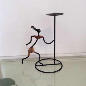 Op de afbeelding: Zwarte metalen kaarsenhouder met een gestileerd figuur dat een kaarsenplaat vasthoudt. Het figuur is gemaakt van draad en heeft een bruine accent.