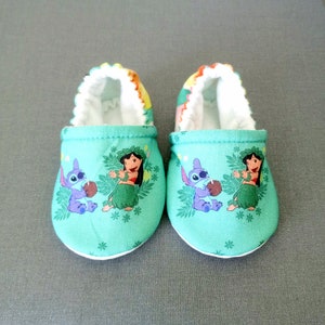 Op de afbeelding: Een paar groene babyschoentjes met een witte rand. De schoentjes hebben een print van de personages Lilo en Stitch uit de Disney-film.