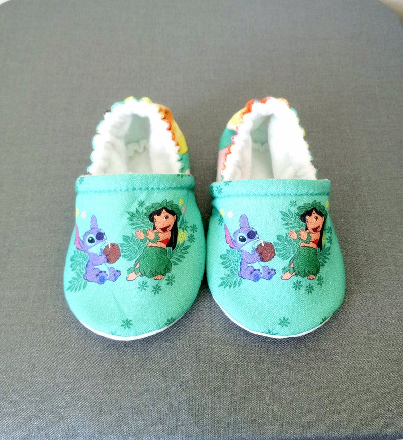 Op de afbeelding: Een paar groene babyschoentjes met een witte rand. De schoentjes hebben een print van de personages Lilo en Stitch uit de Disney-film.