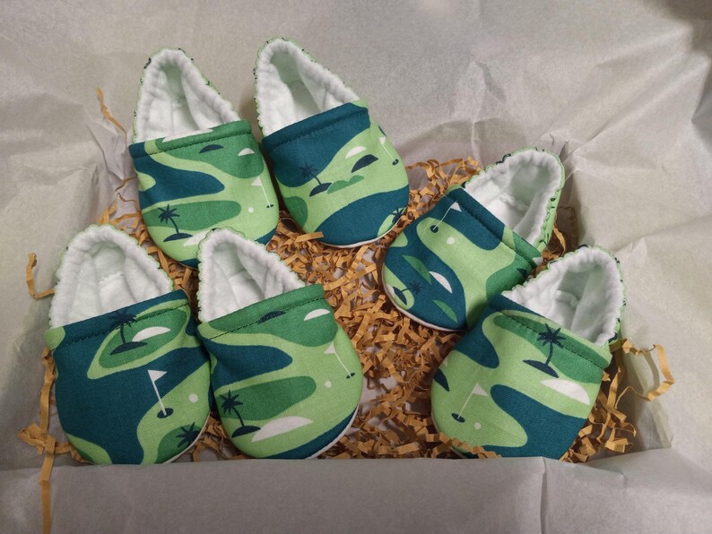 Puede incluir: Seis patucos de beb&eacute; con dise&ntilde;o de campo de golf. Los patucos presentan un estampado verde y azul con forro blanco. Los patucos est&aacute;n colocados en una caja con papel triturado.