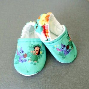 Op de afbeelding: Een paar groene babyschoentjes met een witte rand. De schoentjes hebben een print van Lilo en Stitch-personages uit de Disney-film.