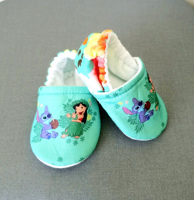 Op de afbeelding: Een paar groene babyschoentjes met een witte rand. De schoentjes hebben een print van Lilo en Stitch-personages uit de Disney-film.
