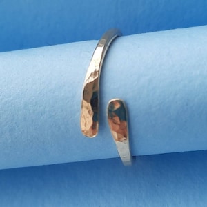 May include: A silver hammered metal ring with a unique open design. The ring is made from a single piece of metal that is bent and hammered to create a unique and modern look.