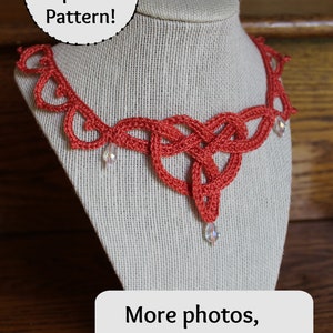 Pode incluir: Um colar de crochê cor de coral com um design de nó e detalhes de cristal. O colar é exibido em um manequim branco. O texto "Updated & Improved Pattern!" está em um círculo acima do colar. O texto "More photos, better diagrams & a video tutorial" está em um retângulo branco abaixo do colar com um ícone de rosto sorridente.
