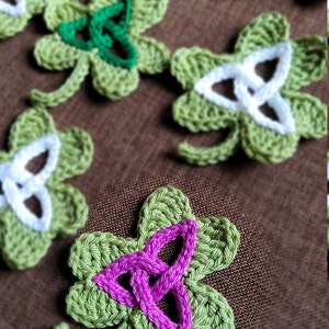 May include: A collection of crocheted shamrock-shaped ornaments in green, white, and pink. The ornaments feature a Celtic knot design.