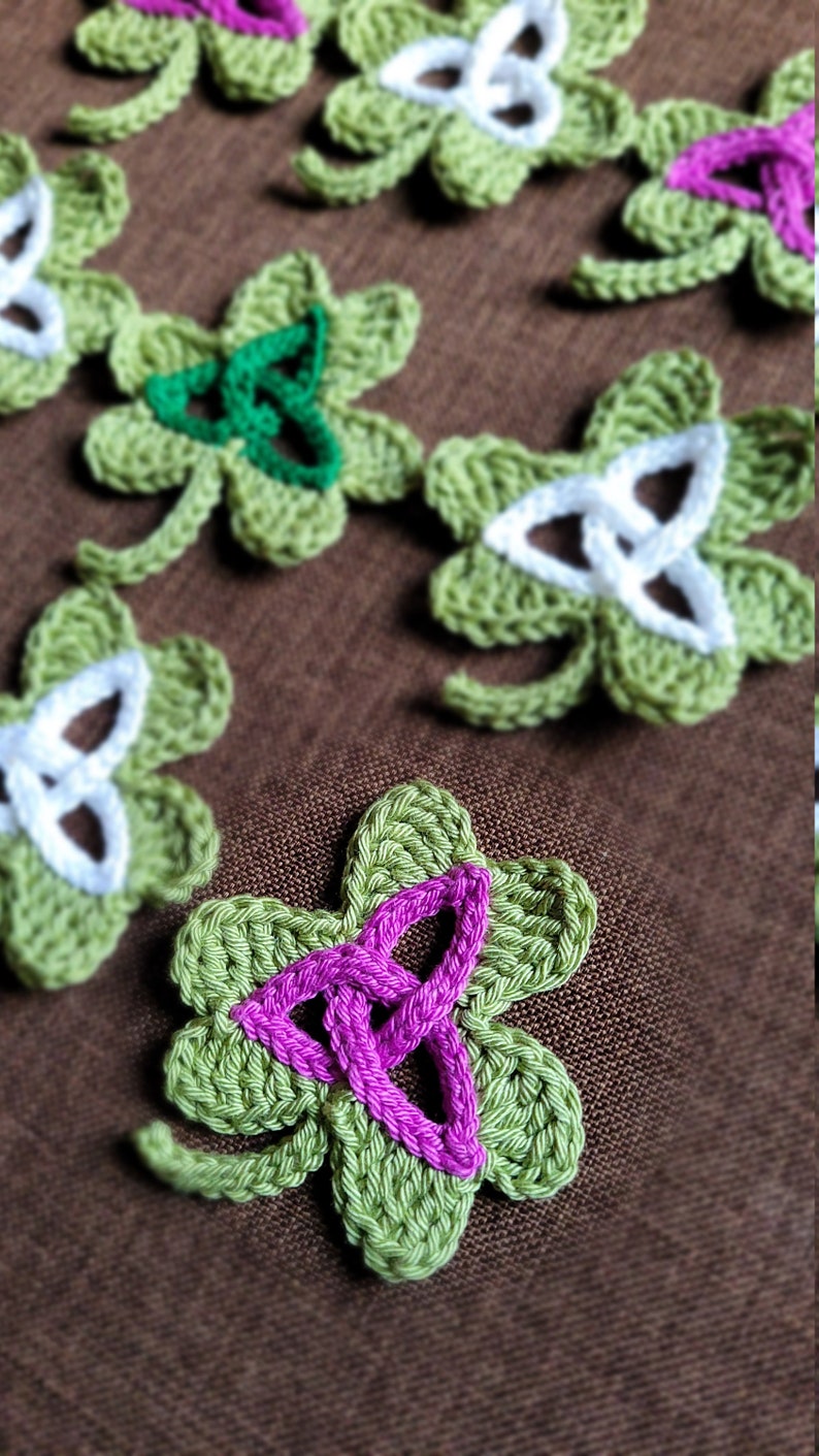 May include: A collection of crocheted shamrock-shaped ornaments in green, white, and pink. The ornaments feature a Celtic knot design.